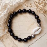 Handcrafted Ancient Cowrie Bracelet with glossy black beads, silver-toned accents, and a natural white cowrie shell.