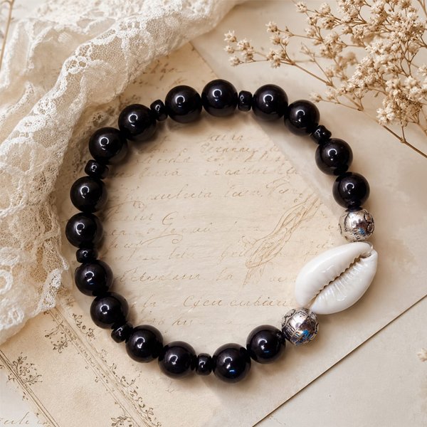 Ancient-Cowrie-Bracelet Handcrafted Ancient Cowrie Bracelet with glossy black beads, silver-toned accents, and a natural white cowrie shell.