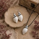 Handcrafted Ivory Conch Pendant Set with matching hook earrings, featuring a glossy white shell-inspired design, adjustable black cord, and elegant vintage styling on an antique background.