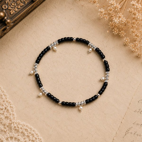 Moon-Drop-Anklet Handcrafted Moon Drop Anklet featuring black glass beads, silver-tone spacer beads, and delicate pearl drop charms, displayed on a soft vintage beige background.