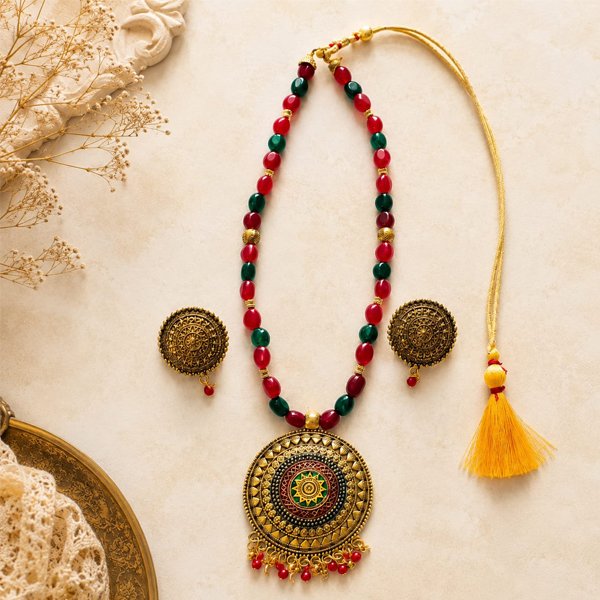 Srida-Mandala-Necklace-Set Srida Mandala Necklace Set with antique gold finish, handcrafted red and green beaded necklace, ornate mandala pendant, and matching earrings for festive and traditional wear.