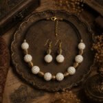 Handcrafted Pearl Dusk Necklace Set with ivory pearl beads, antique gold-tone accents, black thread, and matching earrings displayed in a vintage antique setting.