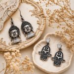 Ancient Whispers combo earrings featuring antique-finish Buddha and Hamsa designs with intricate detailing, displayed on a soft vintage beige background.