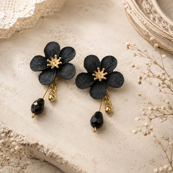 Midnight-Blossom-Earrings Black clay floral oxidised earrings with textured petals, gold-toned flower centers, spiral metal drops, and black beads on a light vintage background.