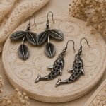 Oxidised silver Bel Patta leaf and dolphin-shaped hook earrings combo set on a vintage beige background.