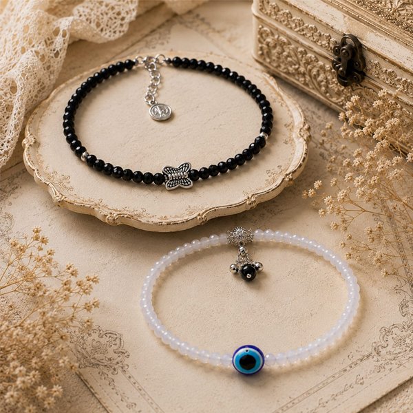 Moon-Whisper-Crystal-Anklet-Combo Handmade women's crystal anklet combo featuring a black butterfly charm anklet and a white evil eye crystal anklet with faceted beads, displayed on a vintage-inspired light antique background.