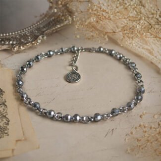 Handcrafted silver-toned faceted beaded anklet with an adjustable chain and vintage coin charm, styled on a soft antique background.