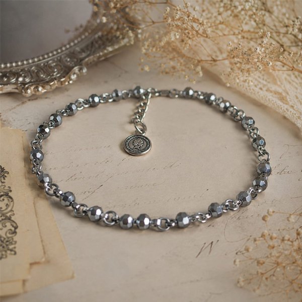 Handcrafted silver-toned faceted beaded anklet with an adjustable chain and vintage coin charm, styled on a soft antique background.
