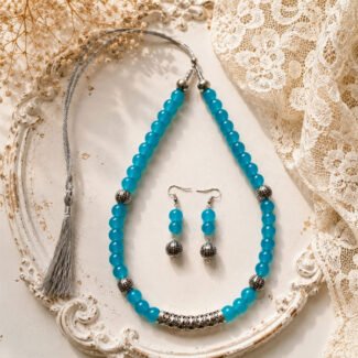 Sky Bloom Beaded Set featuring a handcrafted sky-blue beaded necklace with antique silver-tone accents, adjustable tassel closure, and matching drop earrings on a light vintage background.