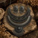 Tribal Bloom Oxidised Necklace Set with matching stud earrings featuring hanging charms in an antique silver finish, displayed on a vintage rustic background.