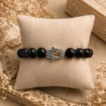 Black beaded Hamsa bracelet with an antique silver-tone Hamsa charm, arranged in a vintage setting.
