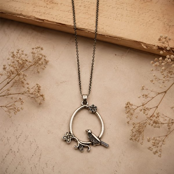 Antique silver Blooming Bird Pendant with a delicate floral vine, oval frame, and detailed bird charm on a dark chain, styled on a soft vintage beige background.