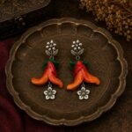 Blooming Palash Clay Earrings featuring handcrafted orange-red Palash flower petals with green clay leaves, oxidised silver floral stud tops, and dangling oxidised flower charms. Lightweight artisan earrings displayed on a vintage antique tray.