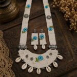 Handmade Blue Blossom Cowrie Cloth Necklace Set featuring embroidered blue floral motifs, oxidised metal accents, cowrie shells, and matching long earrings.